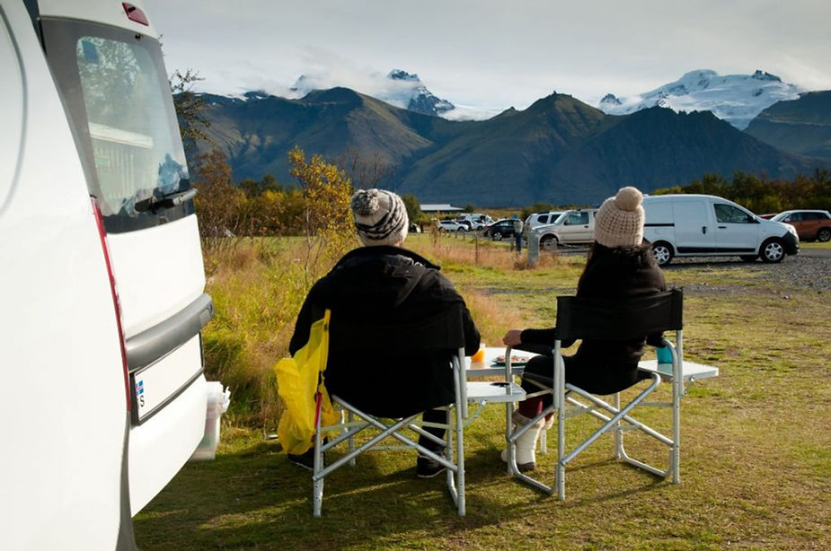 Campeggio di Skaftafel Coppia a un tavolino accanto al camper nel campeggio di Skaftafell, vista su montagne e ghiacciai del Vatnajökull.
