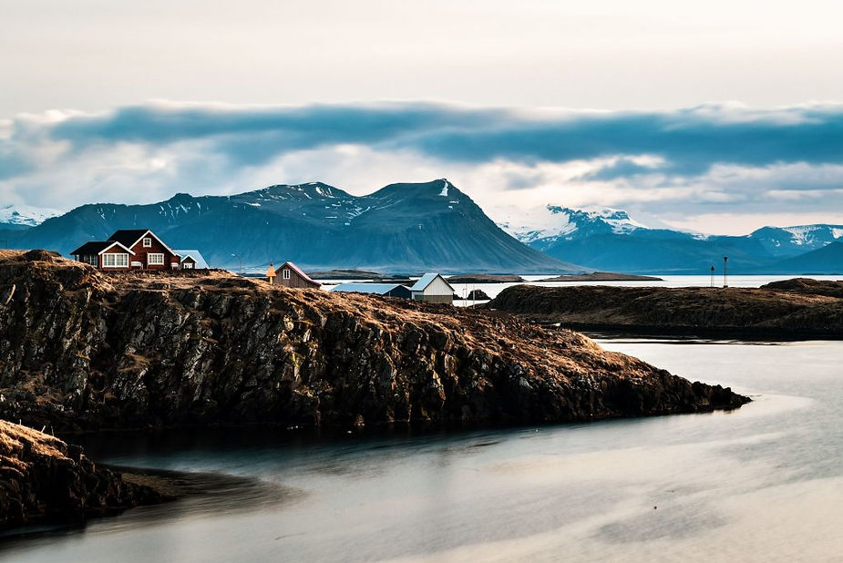 Case sulla costa di Stykkishólmur Case sulla costa di Stykkishólmur affacciate su isole rocciose e fiordo calmo, montagne innevate all’orizzonte.