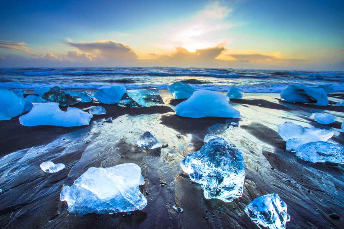 Blocchi di ghiaccio blu sulla sabbia nera della Diamond Beach all&rsquo;alba, riflessi sull&rsquo;oceano vicino alla laguna glaciale di J&ouml;kuls&aacute;rl&oacute;n.