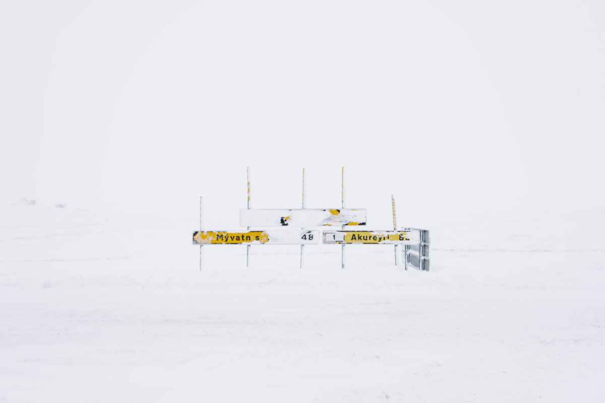 Cartelli stradali verso M&yacute;vatn e Akureyri quasi sommersi dalla bufera; visibilit&agrave; minima e paesaggio completamente bianco nel nord dell&rsquo;Islanda.