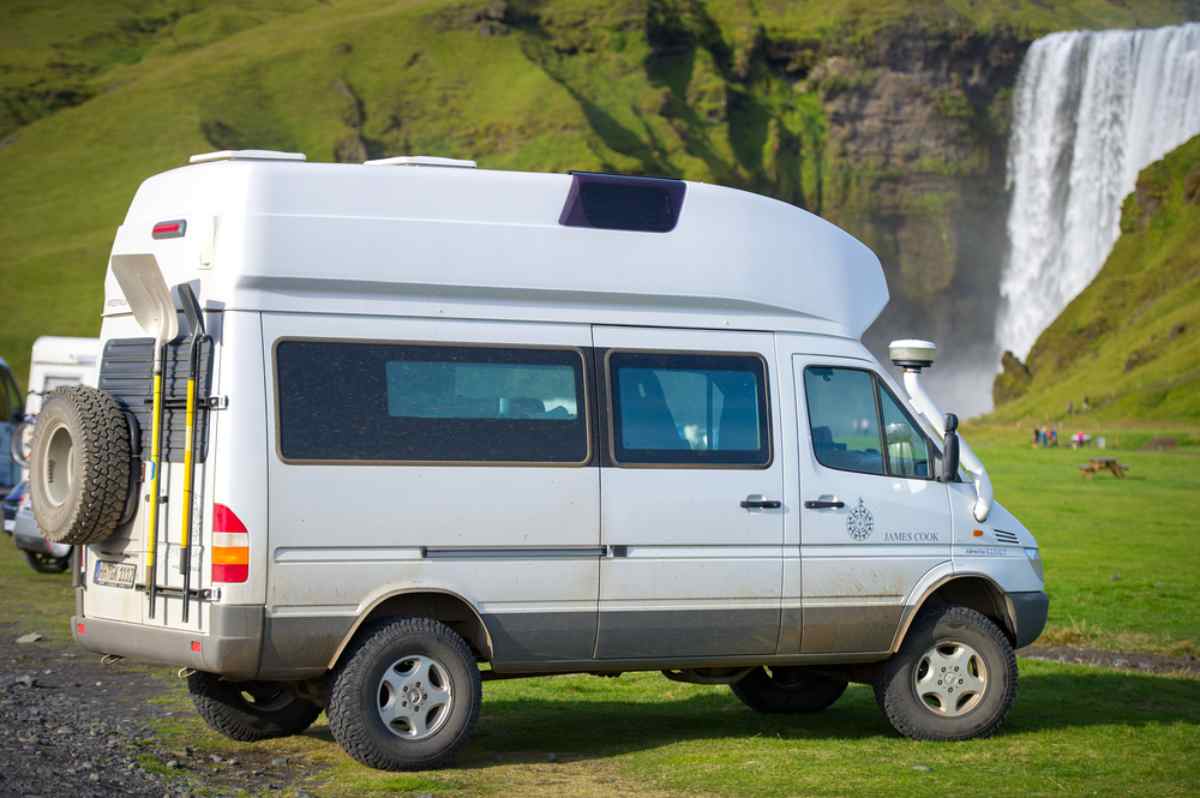 Campervan sostato su prato verde con grande cascata islandese sullo sfondo.