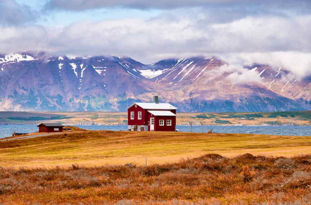Casetta rossa isolata su fiordo islandese con montagne innevate sullo sfondo.