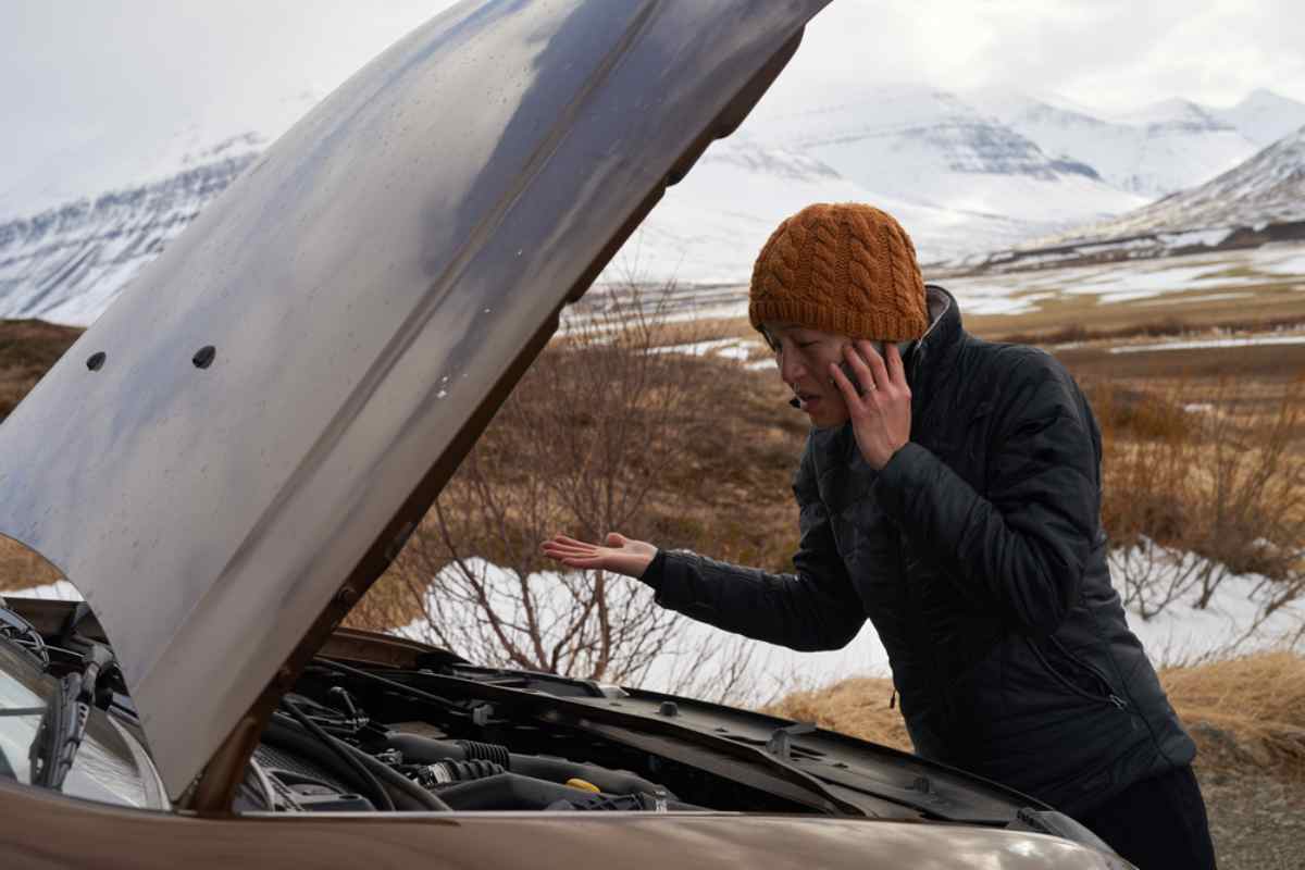 Guasto in montagna Donna al telefono con cofano dell’auto aperto in paesaggio innevato.