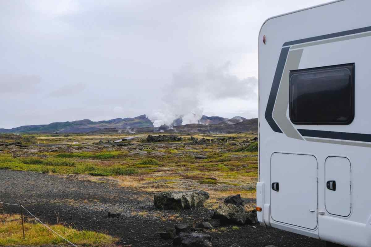 Camper parcheggiato in paesaggio vulcanico d&rsquo;Islanda con fumarole geotermiche e colline sullo sfondo.
