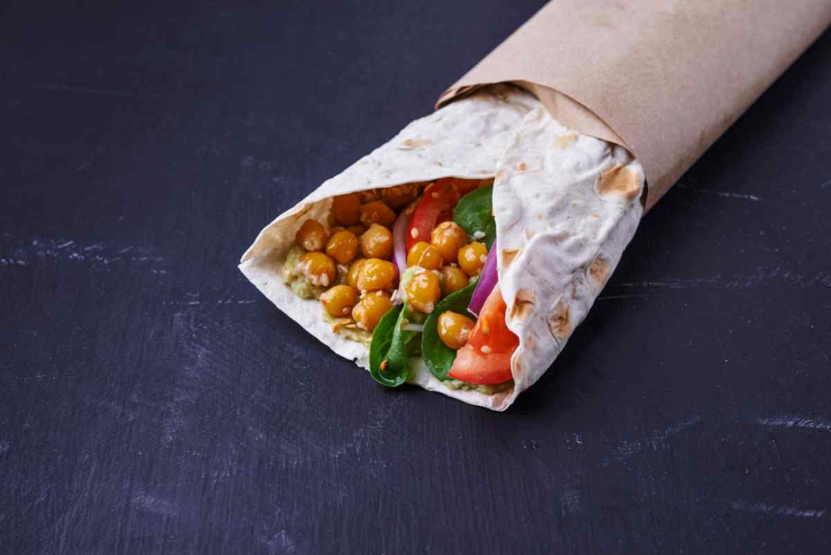 Piadina arrotolata con ceci, pomodoro, spinaci e cipolla rossa, pronta per il pranzo.
