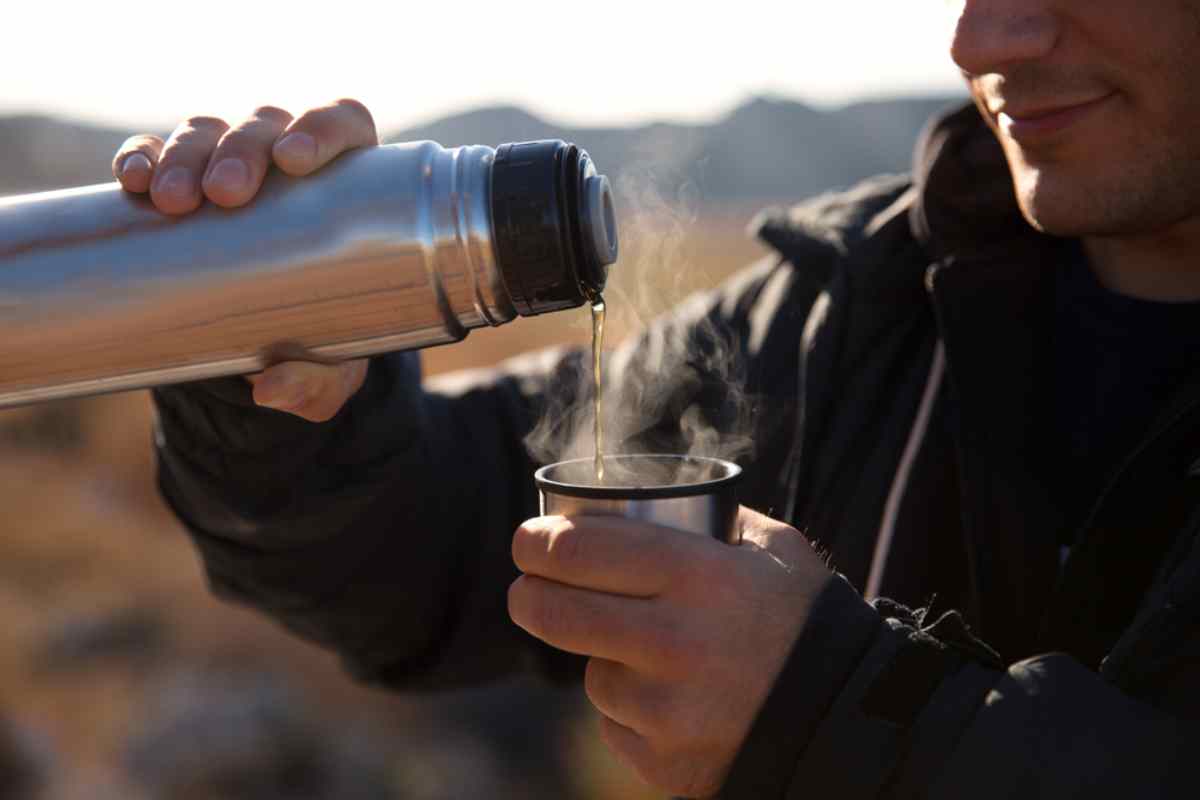 Mano che versa una bevanda fumante da un thermos in una tazza durante la sosta.